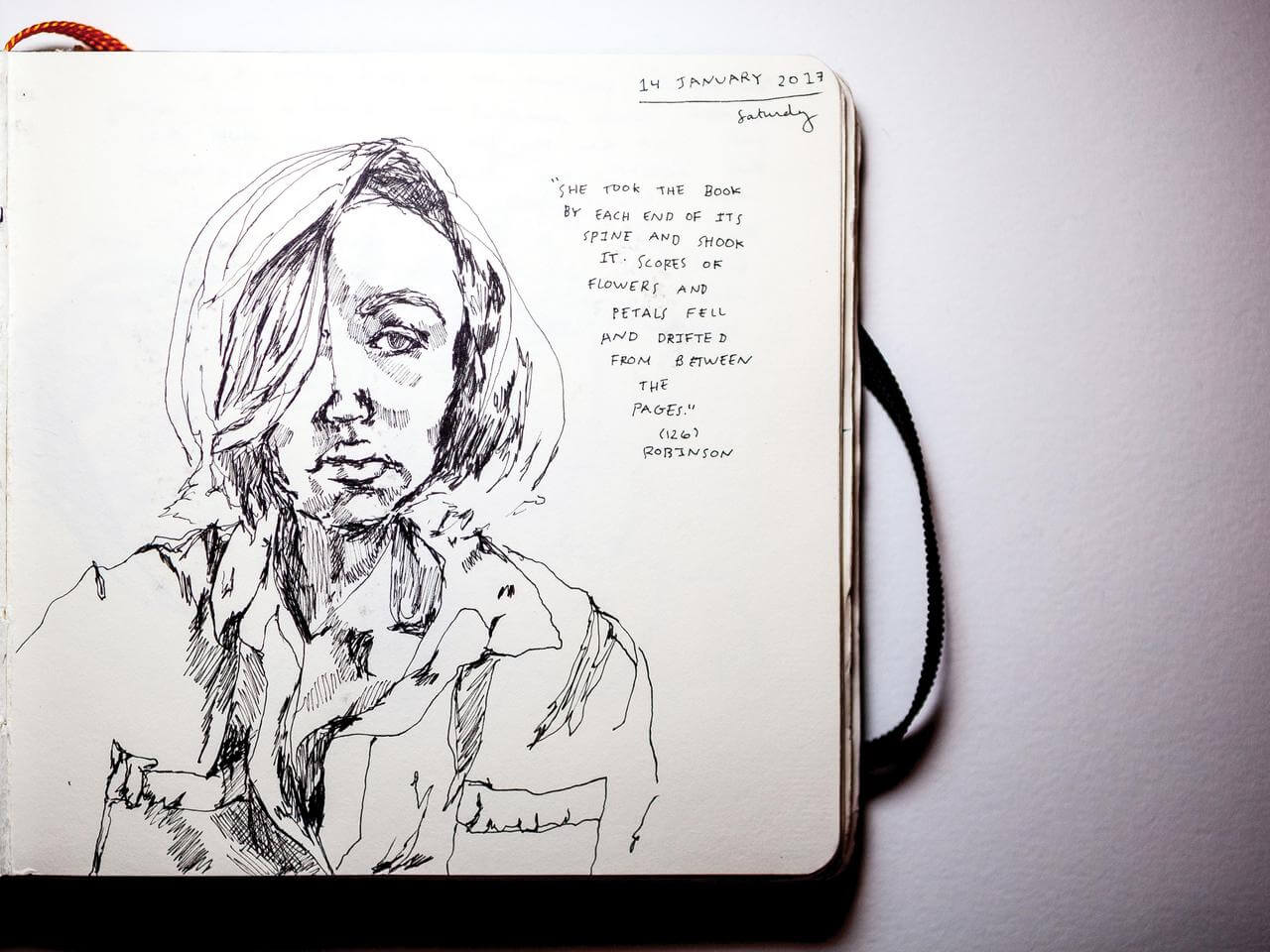 An inked self portrait from the notebook of Sarah Nourie. Next to the portrait is a handwritten quote: "She took the book by each end of its spine and shook it. Scores of flowers and petals fell and drifted between the pages."