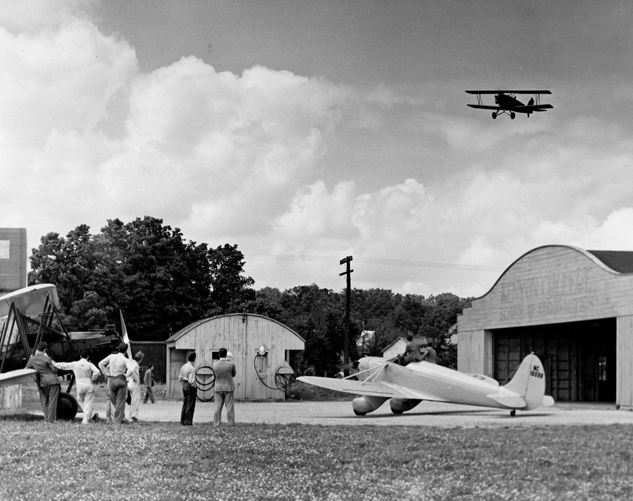 Men watch a biplane fly over the hangar at the Kenyon College School of Aeronautics.
