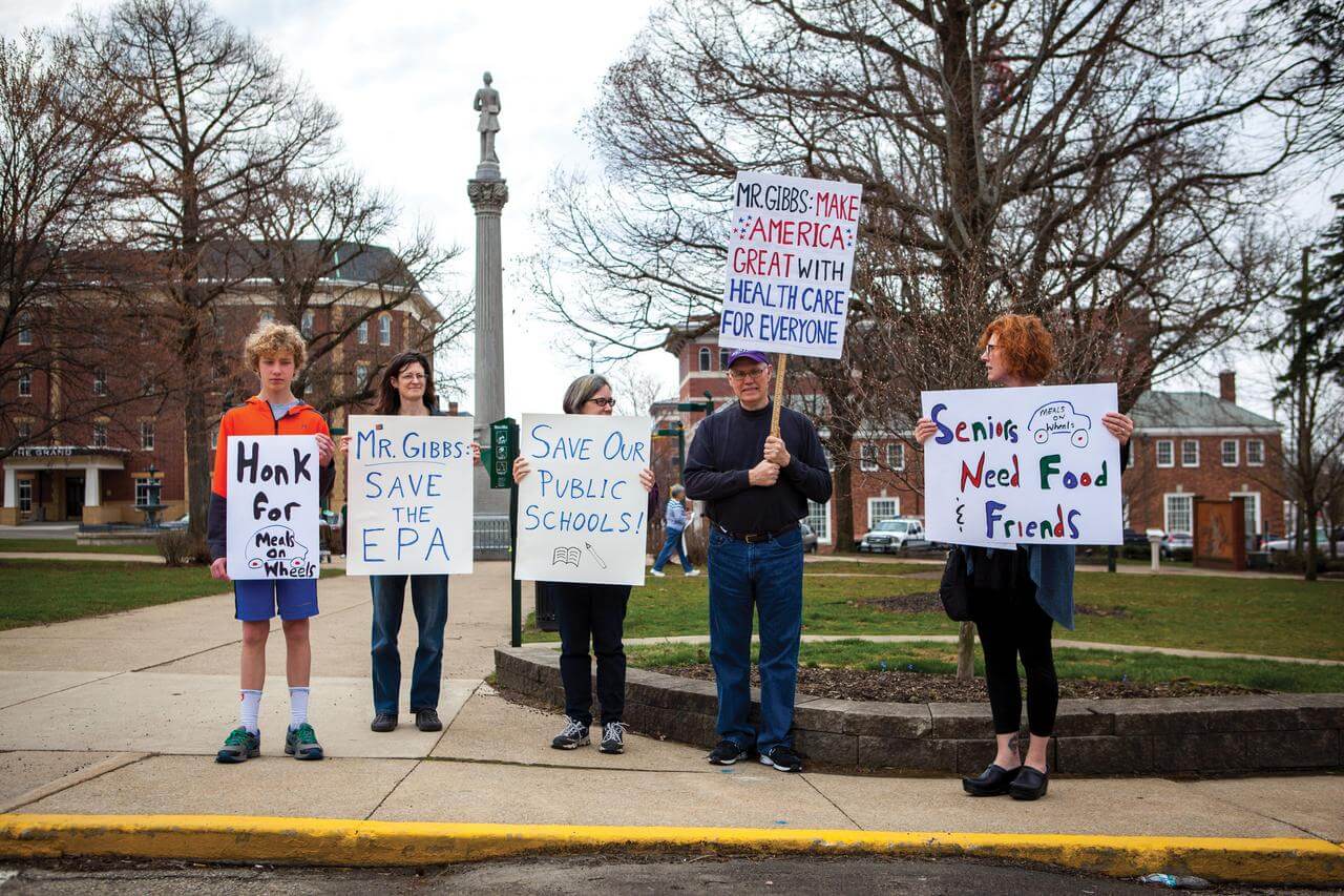 Protesters demonstrate in the Mount Vernon town square, holding signs calling for the protection of public schools, the Environmental Protection Agency, Meals on Wheels, and health care.